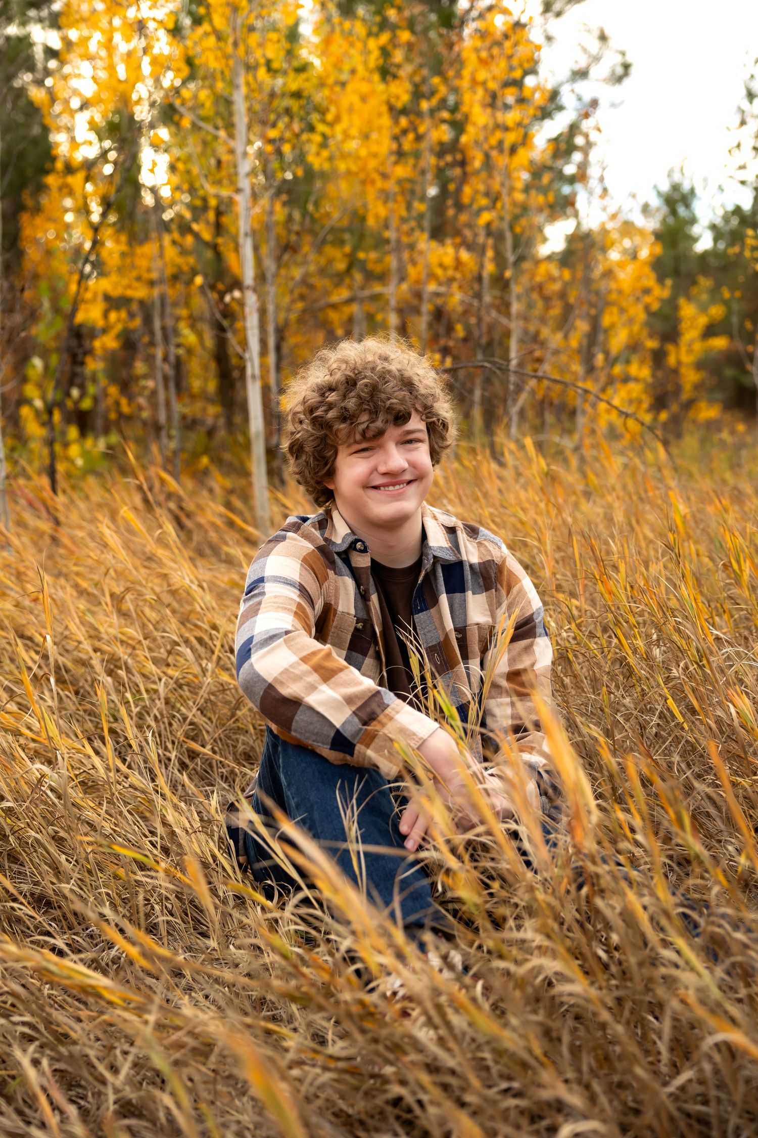 A person in a plaid flannel shirt sits among golden autumn grasses during a fall photoshoot.