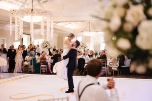 Wedding reception setup in an elegant white ballroom with crystal chandeliers and round tables decorated with floral centerpieces.