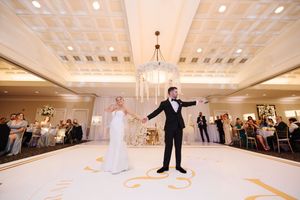 Wedding couple performs dramatic dance moves on an elegant white ballroom floor with chandeliers above.
