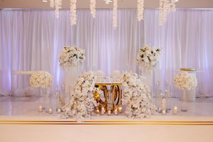 Elegant white wedding reception hall with crystal chandeliers, draped fabric, and floral centerpieces on round tables.