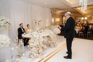 An elegant white wedding reception venue decorated with floral arrangements and white draping.