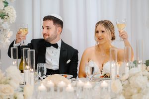 A wedding reception table setting with white floral centerpieces and glowing candles.