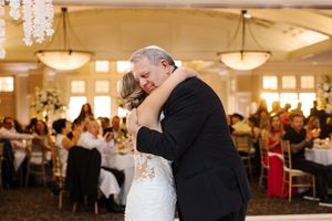 A couple shares a romantic dance at an elegant wedding reception in a grand ballroom with warm lighting.