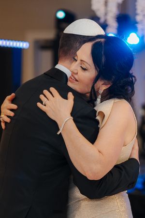 A couple embraces during their first dance at a wedding reception with blue lighting in the background.