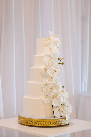 Elegant white wedding cake decorated with cascading white orchids and a gold detailed base trim.