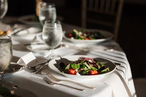 Elegant restaurant table setting with white linens, wine glasses, and fresh salad plates in moody lighting.