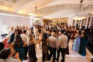 Wedding guests dance and celebrate together in an elegant ballroom with chandeliers and white decor.