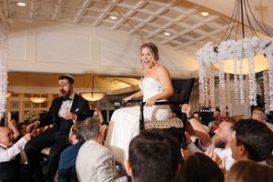 Wedding guests dancing and celebrating on a dance floor at an elegant reception venue with chandeliers overhead.