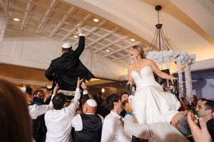 Joyful celebration at a wedding reception as guests dance with their arms raised in an elegant ballroom.