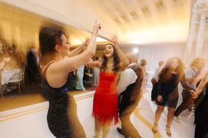 People dancing and celebrating at a party with someone in a red dress in the center of a brightly lit room.