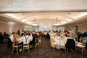 Panoramic view of an elegant wedding reception hall with white chairs, floral centerpieces, and crystal chandeliers.