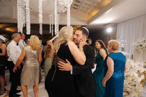 Wedding guests dance and celebrate together on a dimly lit dance floor under crystal chandeliers at an elegant reception.