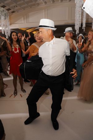 Dancers performing energetic swing dance moves at a formal event with a crowd watching in the background.