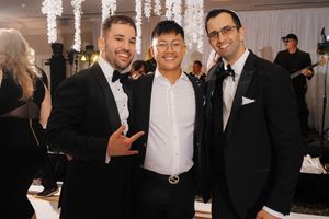 A group of people in formal attire socializing at an elegant event with crystal chandeliers overhead.