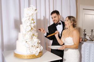 A wedding couple cuts into their elegant white and gold tiered cake during their reception celebration.
