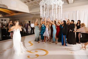 Wedding guests gather excitedly beneath a crystal chandelier as the bride tosses her bouquet during the reception.