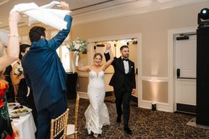 Newlyweds make their grand entrance at wedding reception while guests wave napkins in celebration.