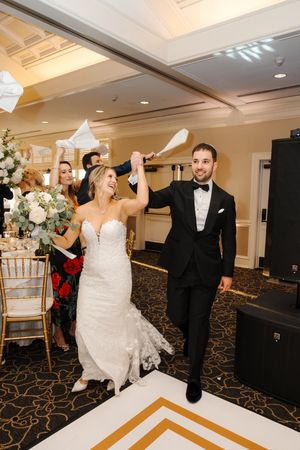 Wedding couple dances together on a white dance floor in an elegant ballroom with decorative carpeting and lighting.