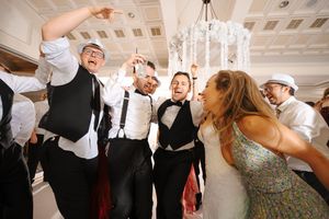 Wedding party guests dancing and celebrating together on the dance floor at a reception under a crystal chandelier.
