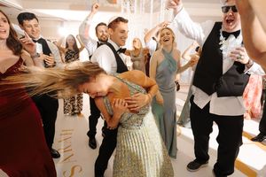Wedding party celebrates on dance floor with guests dancing and cheering during reception celebration.