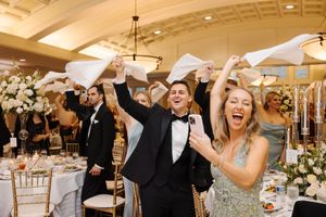 Wedding celebration with guests dancing and raising their arms joyfully in an elegant reception venue.