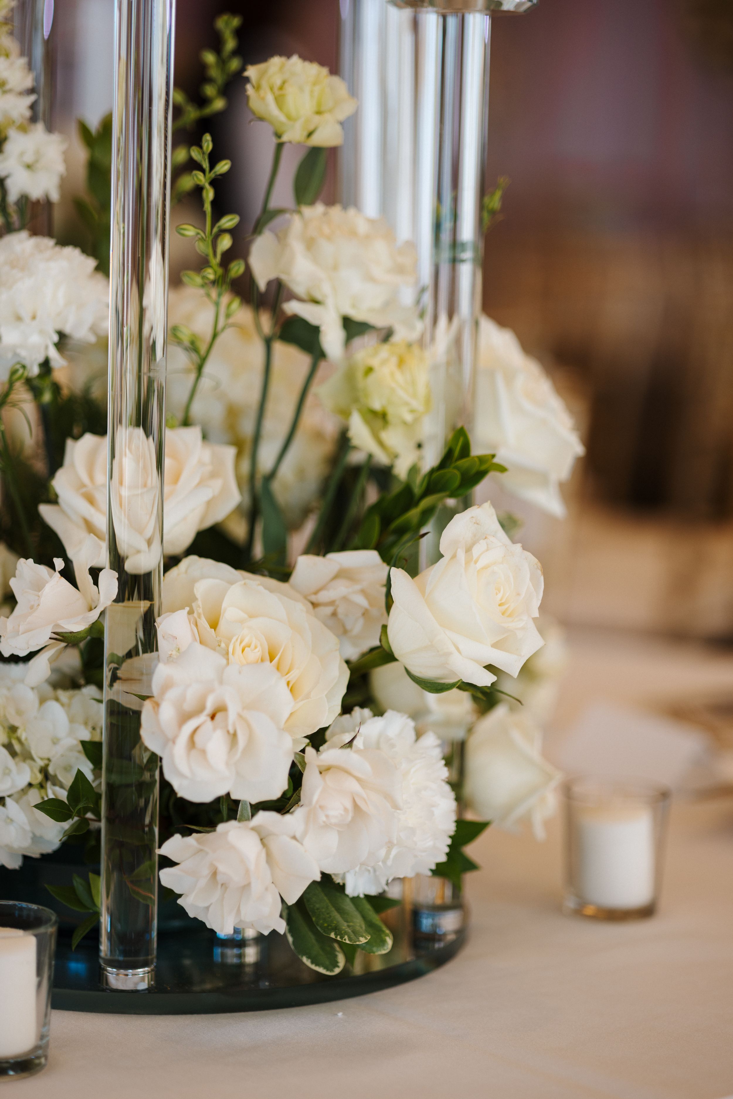 Elegant white carnations and roses arranged in tall glass vases create a sophisticated wedding centerpiece display.