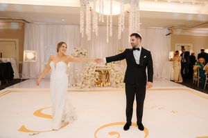 Elegant couple shares their first dance on a white and gold decorated ballroom floor during wedding reception.