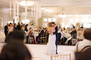 Wedding guests dance and celebrate together in an elegant white ballroom with chandelier lighting.