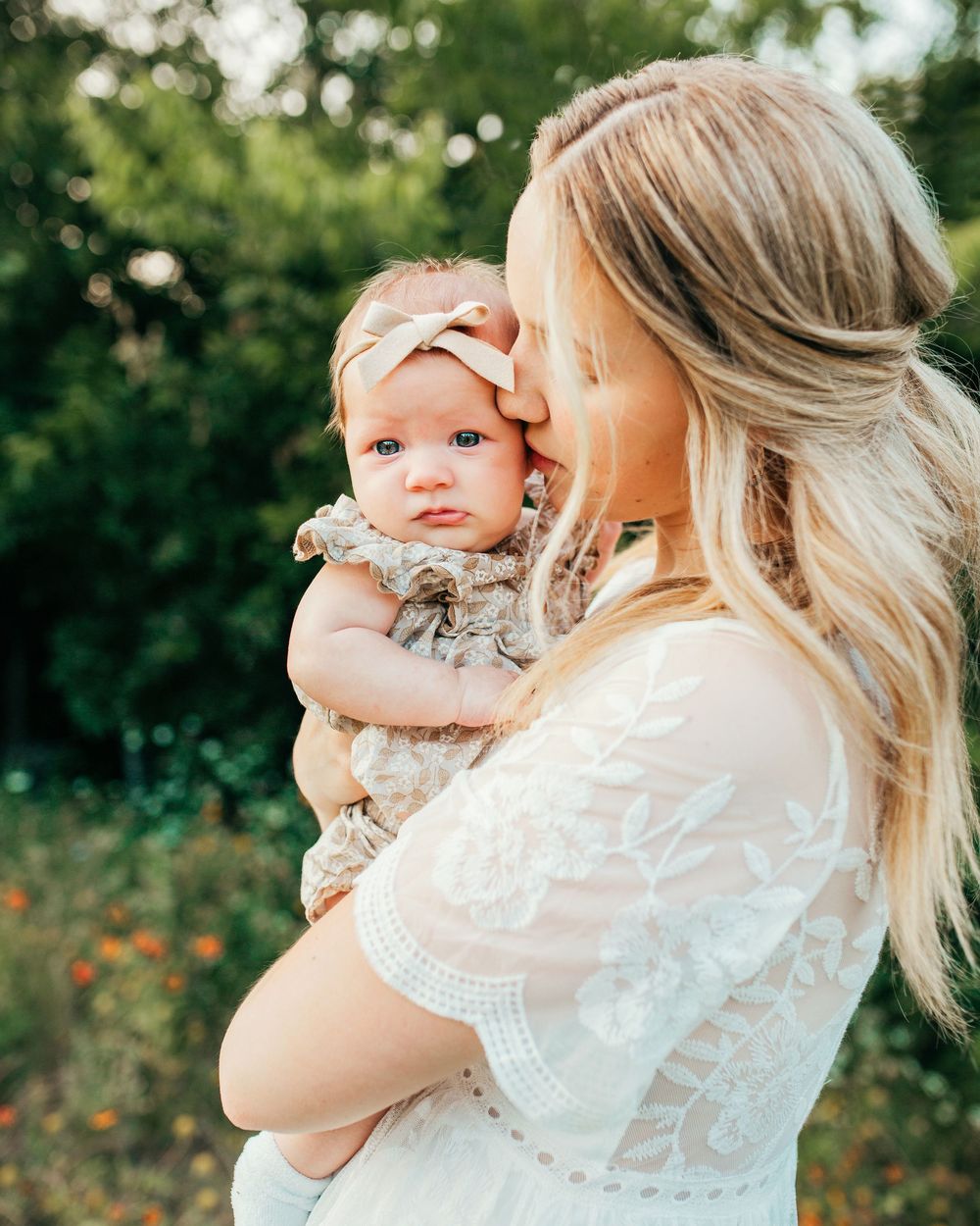 A tender moment with mother and her infant captured in a field with a white lace dress and gentle summer lighting in Fort Worth