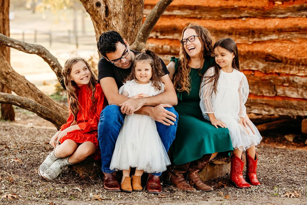 Family sits together on a large rock wearing coordinated autumn outfits in warm sunlight at sunset in Colleyville, TX