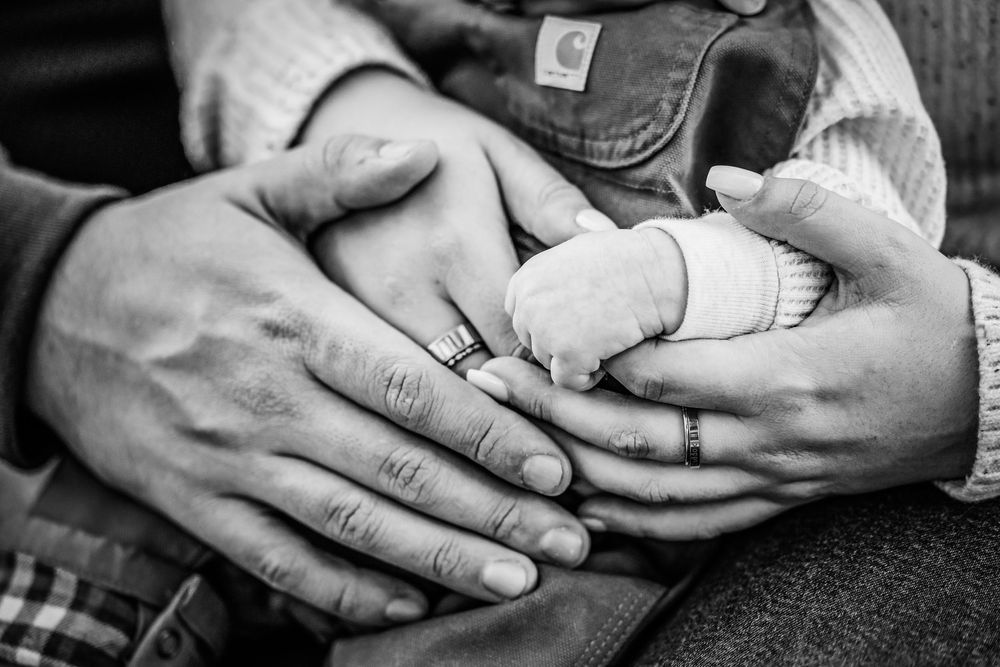 Black and white close-up of hands gently holding a newborn baby's hands in a tender family moment in Keller, TX