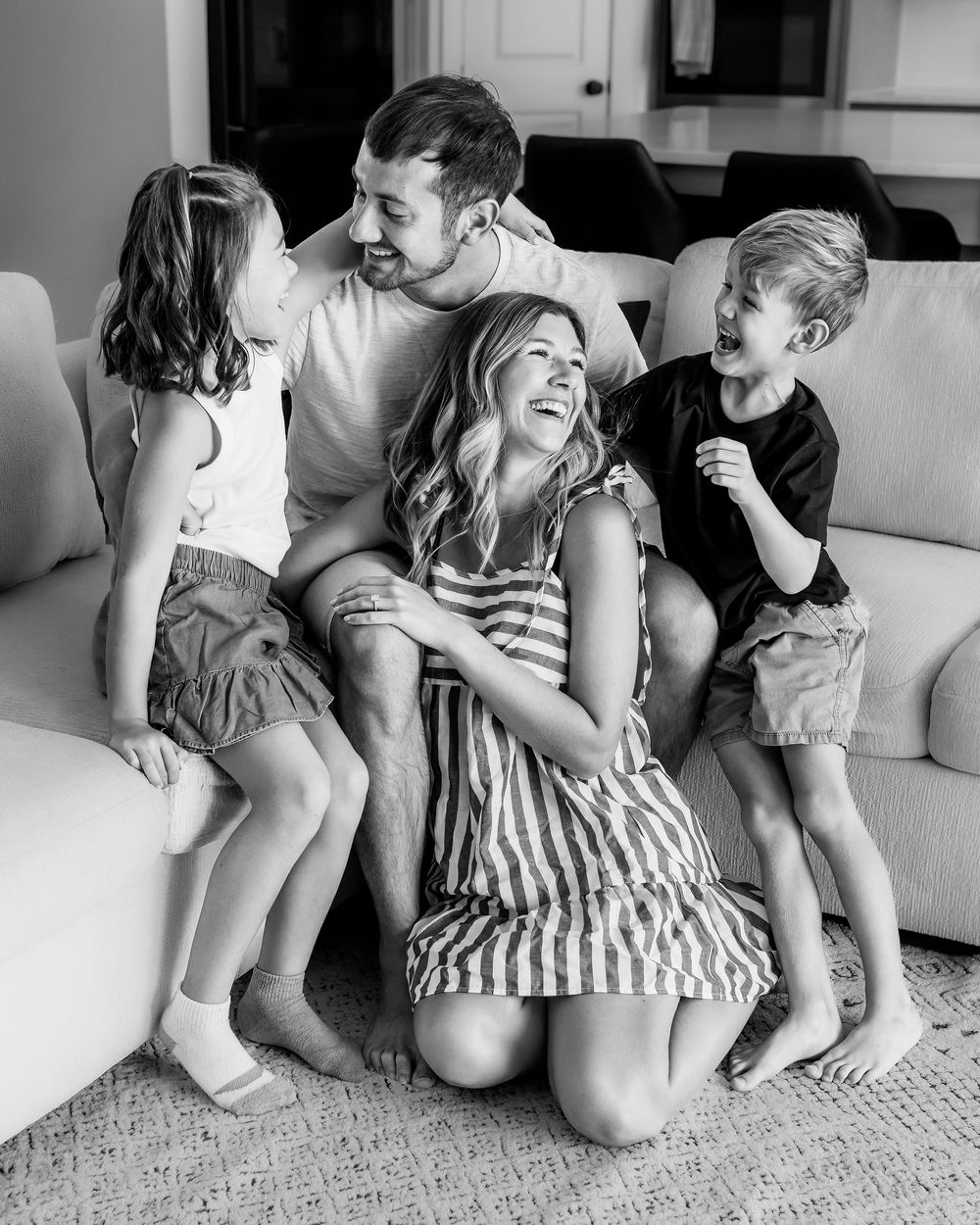 A black and white photo showing candid moments of family affection and laughter on a couch during their in-home session in DFW