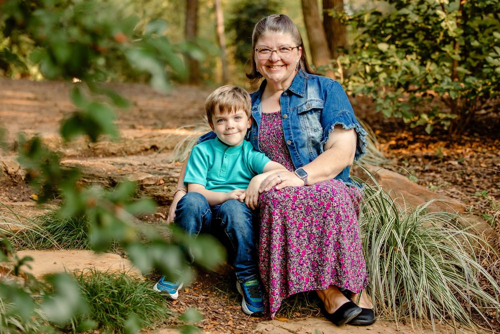 A mother and son sit together on stone steps surrounded by autumn foliage in a garden setting in Grapevine, TX