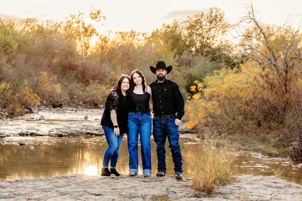 A family poses for outdoor  portraits beside a creek in autumn setting in Fort Worth