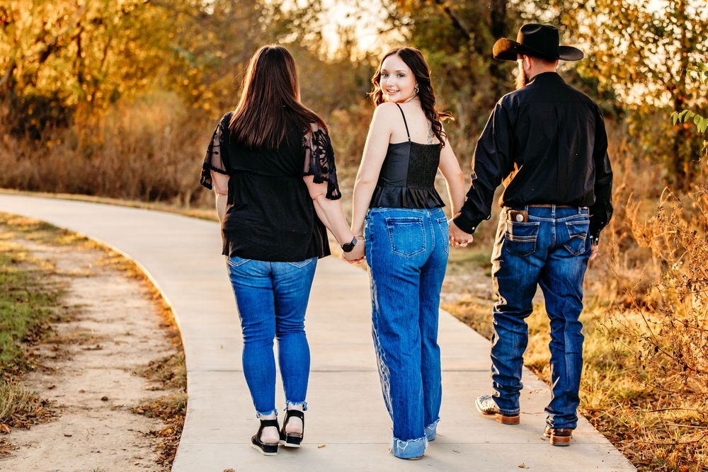 Family of three walk together on a sunlit path during golden hour with autumn foliage in the background in Fort Worth