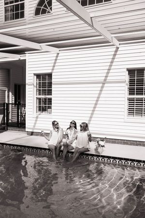 People enjoying a refreshing swim in a pool beside a white house with shuttered windows.