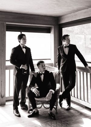 Groomsmen in black tuxedos posing creatively on a wooden deck in a unique horizontal composition.