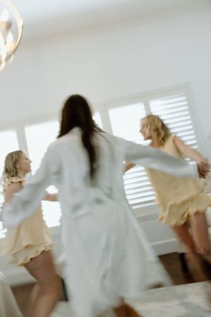 Motion-blurred photo of women dancing and twirling in light-colored dresses.