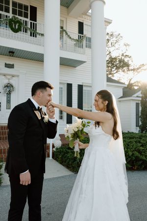 Couple in wedding attire shares playful dance moves outside a white columned building.