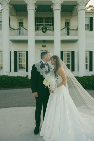 An elegant wedding photoshoot in front of a grand white colonial-style mansion with columns and manicured gardens.