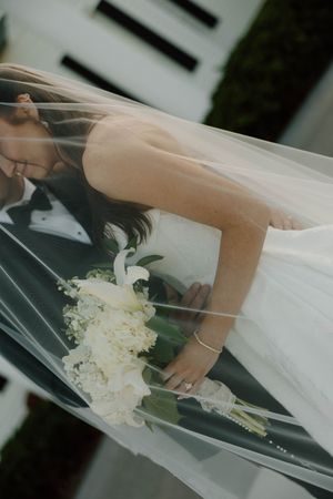 A delicate white bridal veil flows elegantly in the breeze beside a bouquet of white flowers.