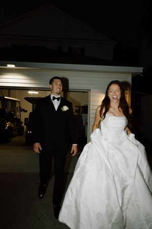 A couple in formal wedding attire walk through a dimly lit indoor venue.