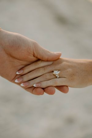 Close-up of hands with engagement ring showing tender moment between couple.