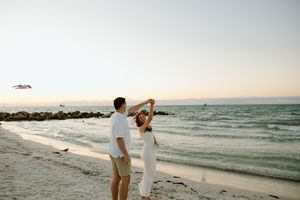 Couple in light colored outfits walking along a beach at sunset.