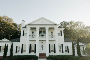 Elegant white antebellum-style mansion with tall columns and black shutters features symmetrical design and cypress trees.