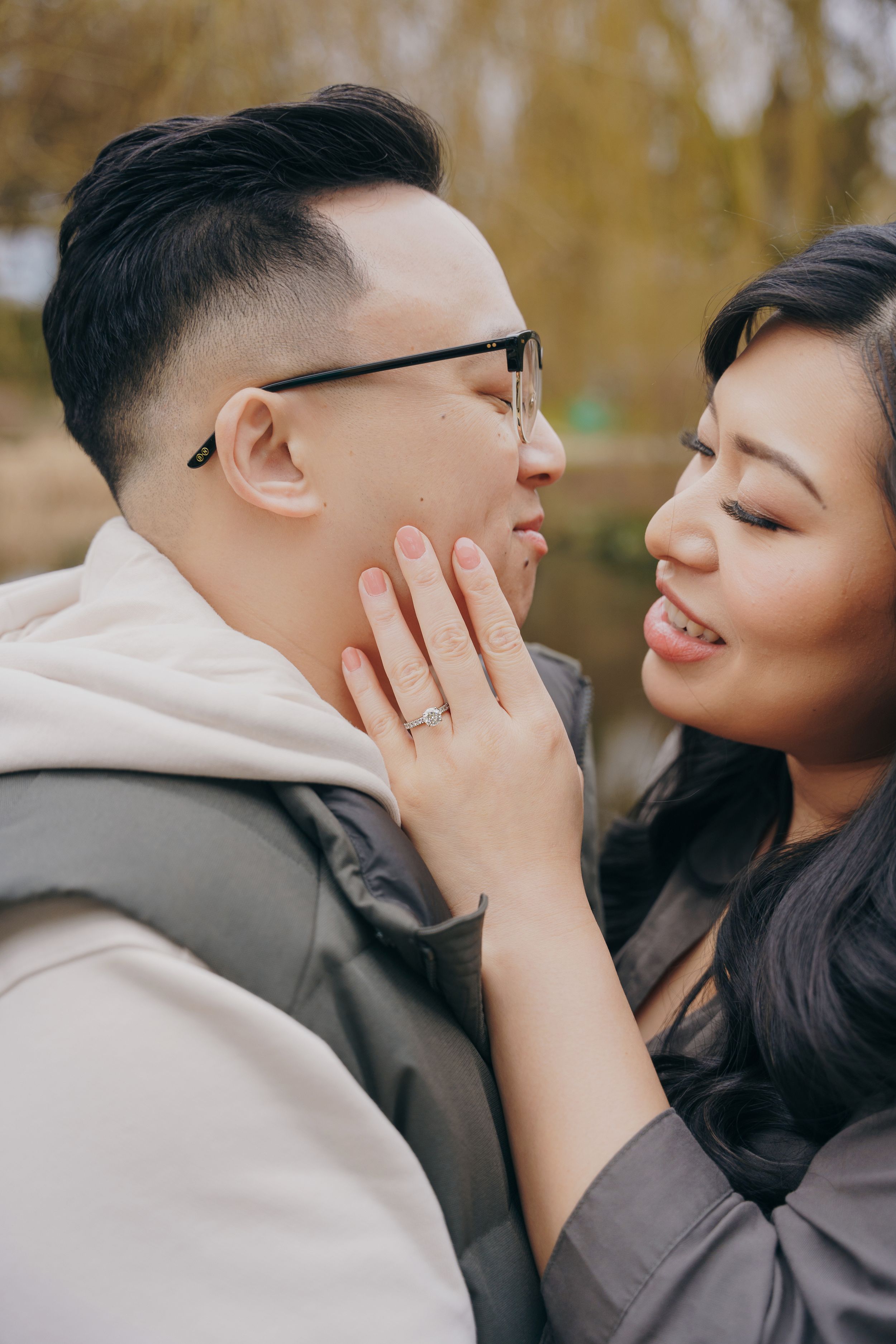 A romantic couple shares an intimate moment outdoors during autumn with one person gently touching the other's face.