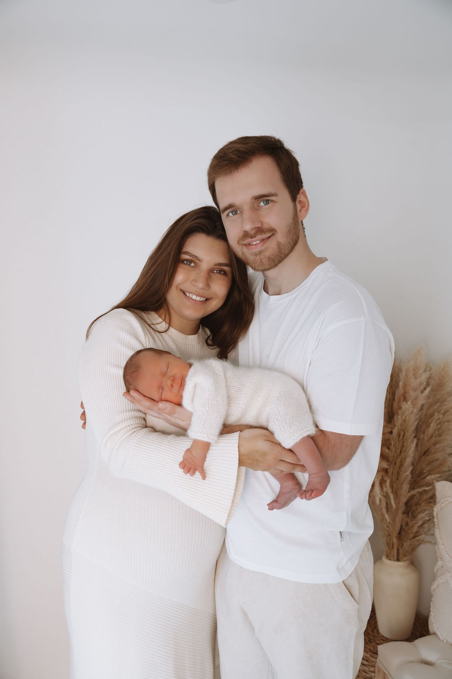 A couple in white outfits poses together against a neutral wall in a series of intimate lifestyle photos.