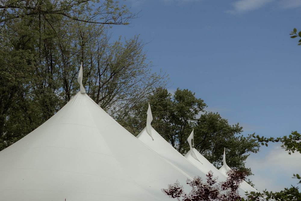 White tent peaks rise against a blue sky with trees visible in the background on a sunny day.