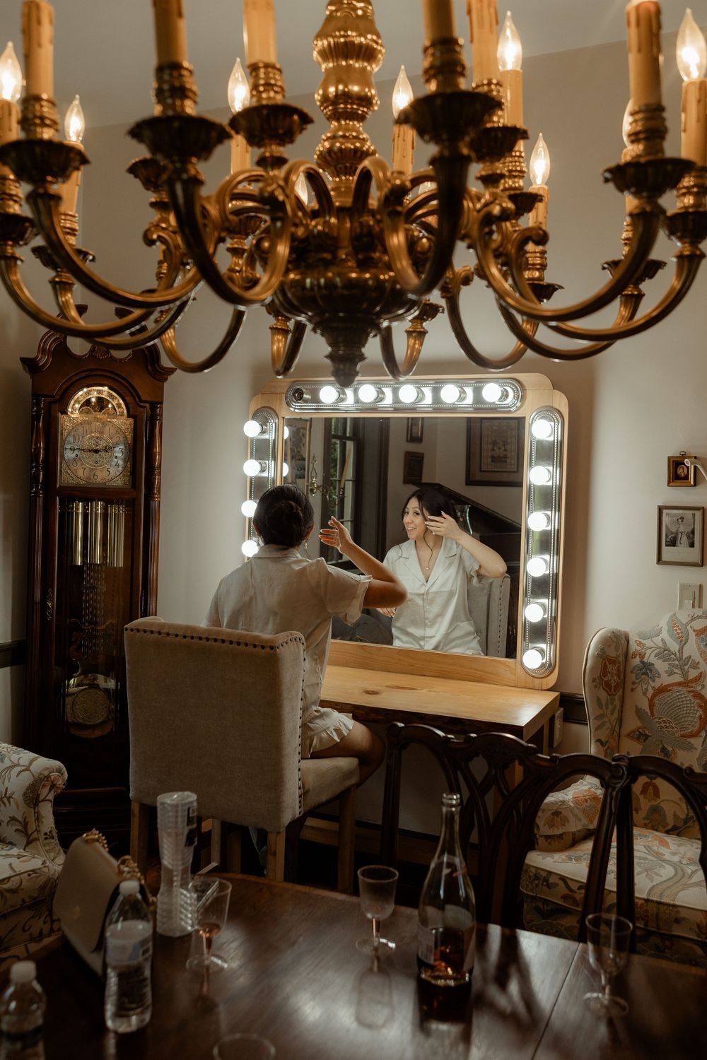 Elegant dressing room with ornate gold chandeliers, illuminated vanity mirrors, and wooden furniture creates a luxurious atmosphere.
