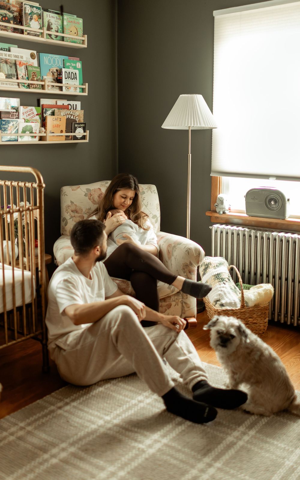 A person sits on the floor of a nursery with a dog while sunlight streams through the window creating warm shadows.